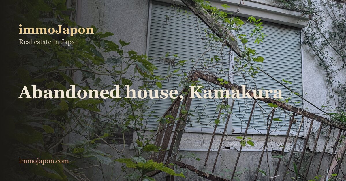 An abandoned house in Kamakura reclaimed by vegetation: cracked white render, a pale blue metal shutter across the window, a collapsed roof with exposed rafters and displaced tiles, a rusted railing fallen across the frame, brambles and dwarf bamboo growing up to the wall