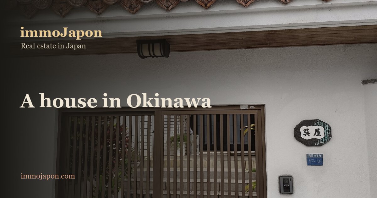 Entrance to a detached house in the Nishihara district of Urasoe, Okinawa: slatted aluminium sliding gate, white rendered boundary wall topped with red Okinawan roof tiles, carved stone nameplate and the block address plate of the fifth chome