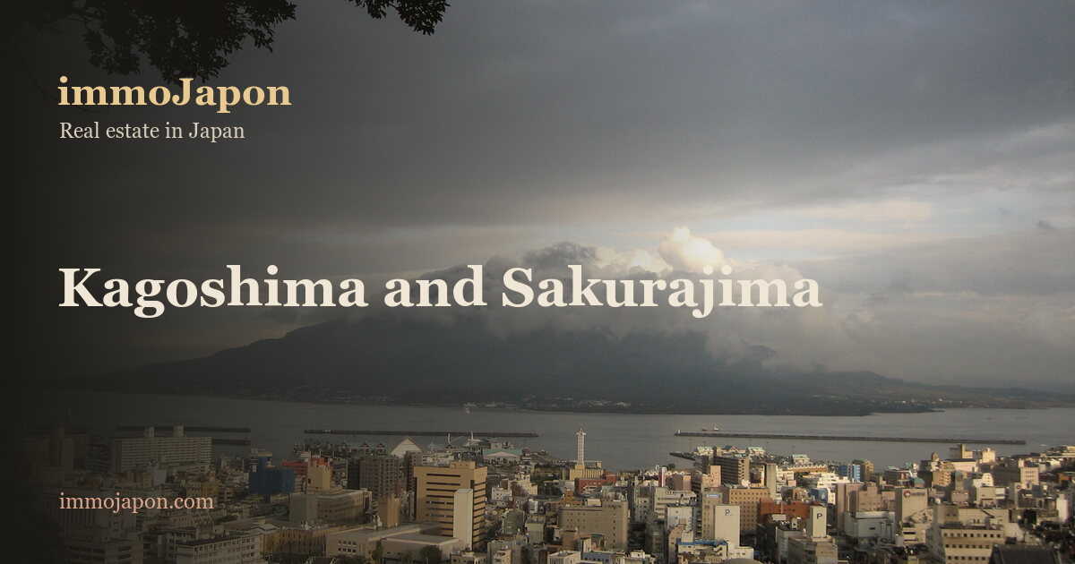 Low-rise apartment blocks and houses of Kagoshima city spread down to the bay, with the Sakurajima volcano rising across the water under a heavy grey sky and a cloud resting on its summit.