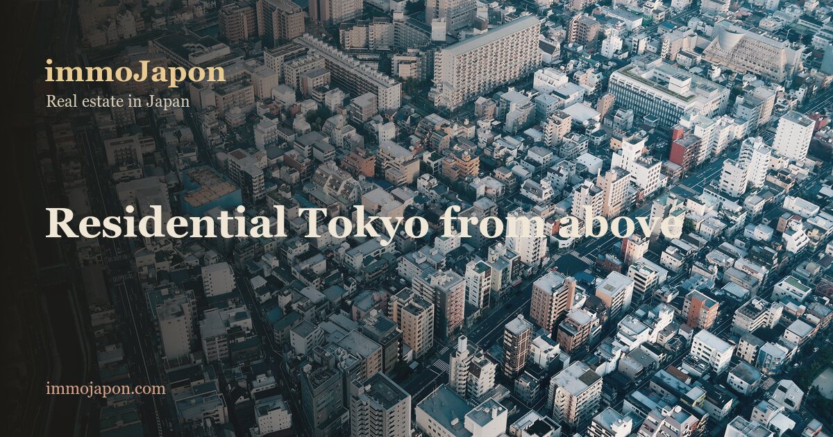 Dense residential Tokyo seen from high above: hundreds of low and mid rise apartment blocks with flat roofs packed edge to edge across the whole frame, narrow streets forming an irregular grid between them, a railway line and a road running diagonally along the lower left corner, and a few taller buildings breaking the roofline. No sky is visible, the built city fills the image.