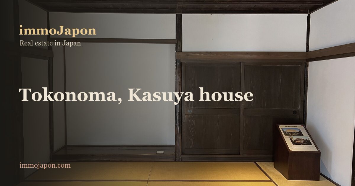 A traditional Japanese room in the former Kasuya house: a tokonoma alcove recessed into the left of the wall, its raised floor edged with a dark timber beam, dark wooden sliding doors to the right, pale tatami matting underfoot and an exposed beam ceiling