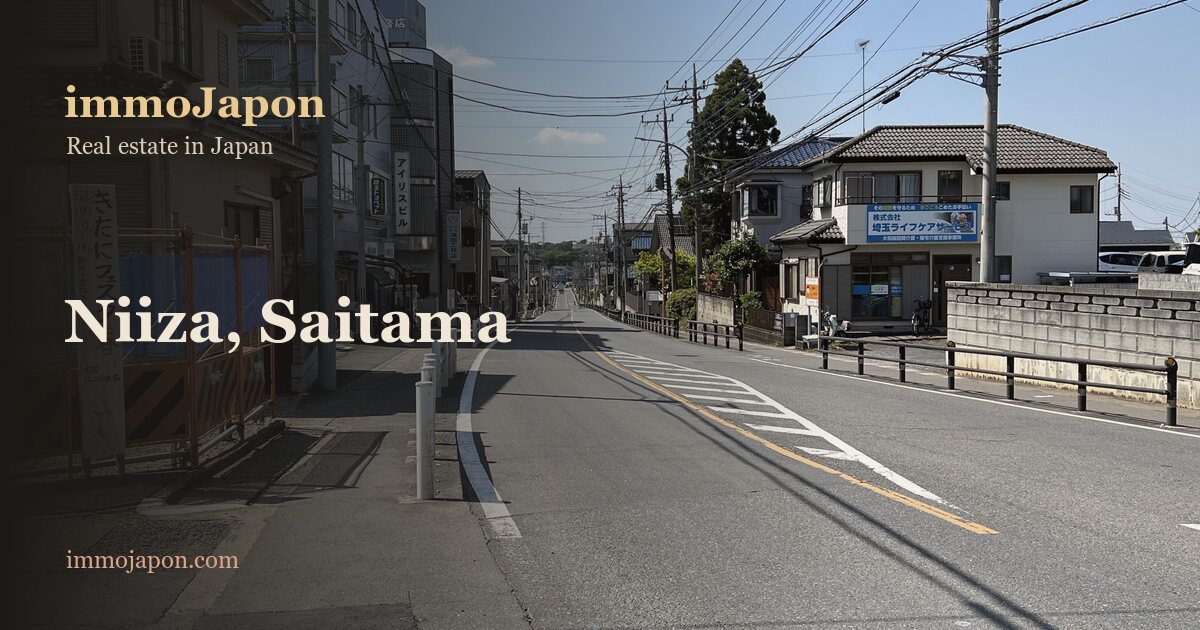 A quiet residential road in Niiza, a commuter town in Saitama on the edge of Tokyo: two-storey detached houses, overhead power lines and a straight two-lane street under a clear blue sky